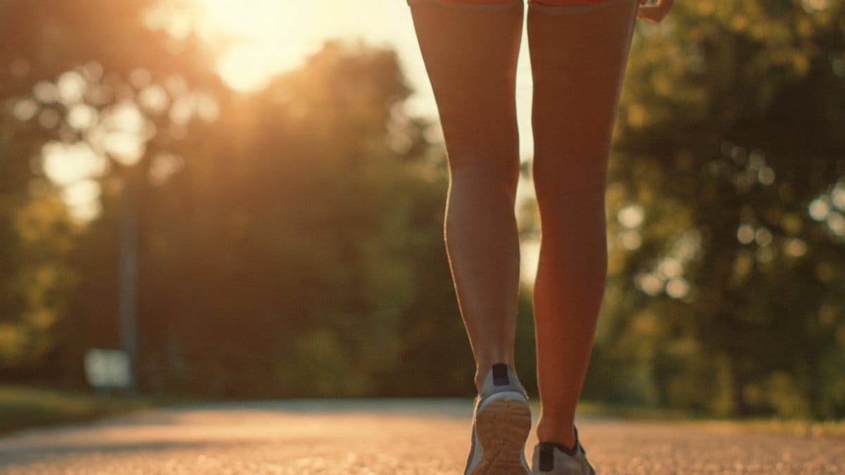 Atrito nas coxas ao caminhar: pernas de pessoa caminhando em trilha de parque ao pôr do sol, de shorts, com as coxas se tocando a cada passo